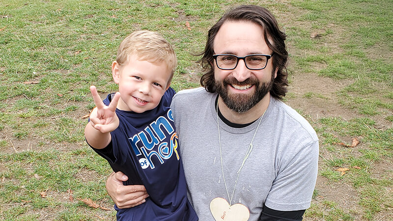 Seattle Children’s Dr. Nick Vitanza kneels in the grass with patient Gavin Nielsen at the annual Seattle Run of Hope.