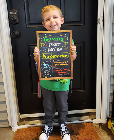 A 5-year-old holds up a First Day of Kindergarten sign