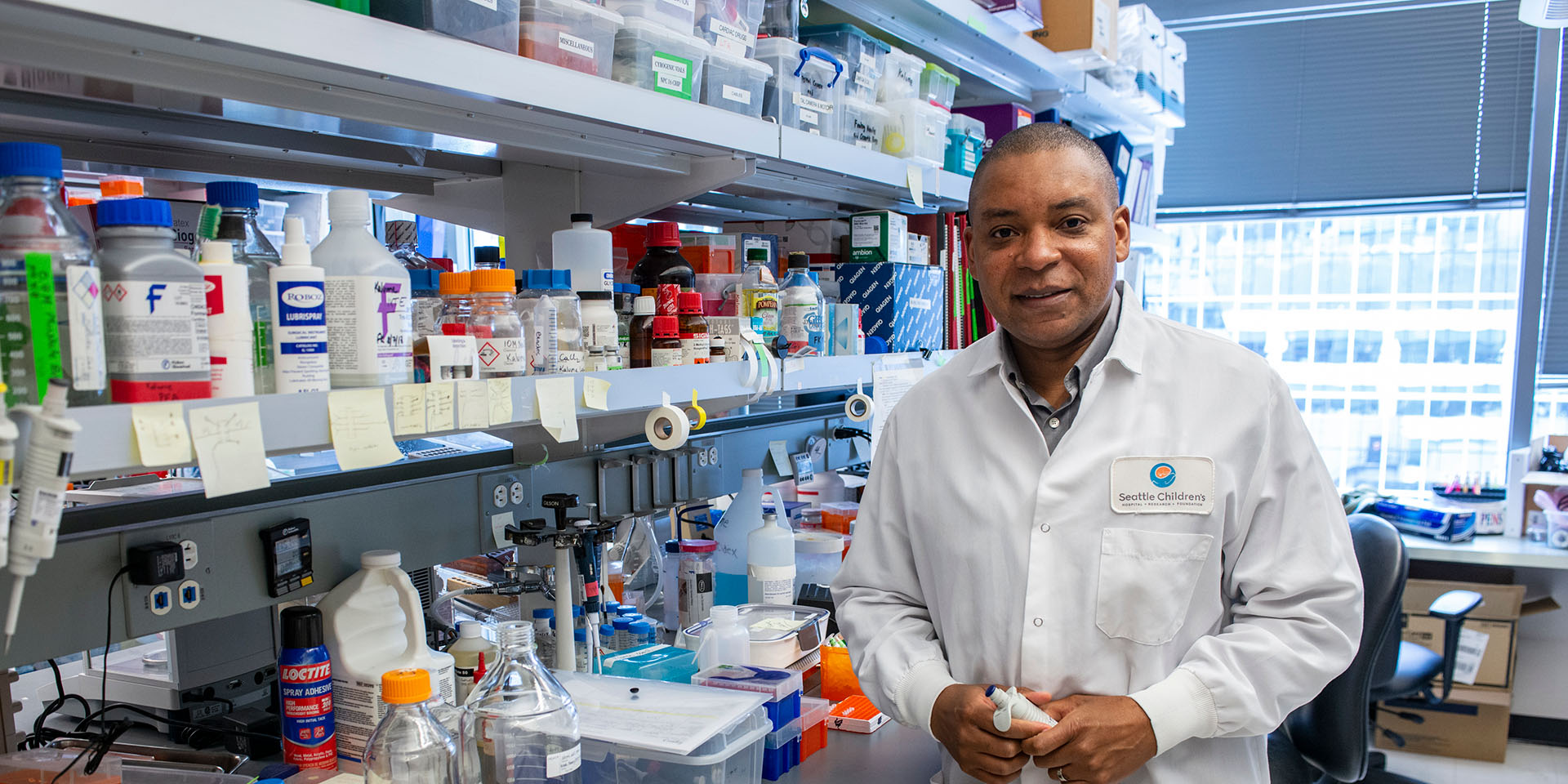 Seattle Children’s Dr. Franck Kalume, wearing a lab coat and holding a pipette, stands in his research lab. 