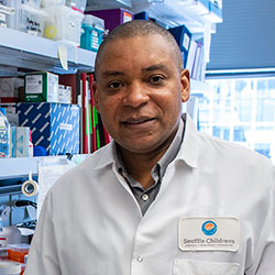 Seattle Children’s Dr. Franck Kalume, wearing a lab coat and holding a pipette, stands in his research lab. 