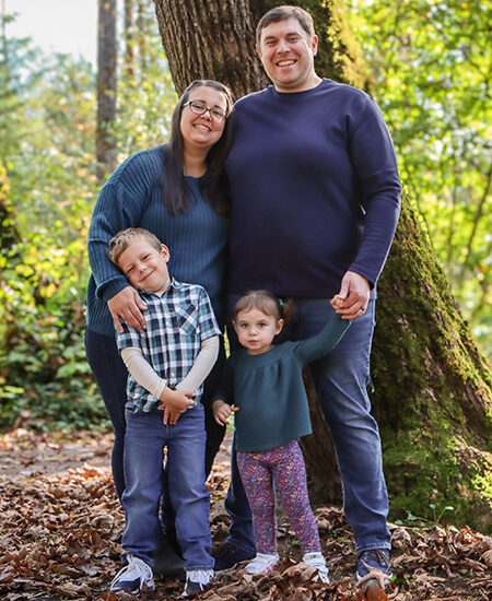 A mother, father, and their son and daughter standing in the woods