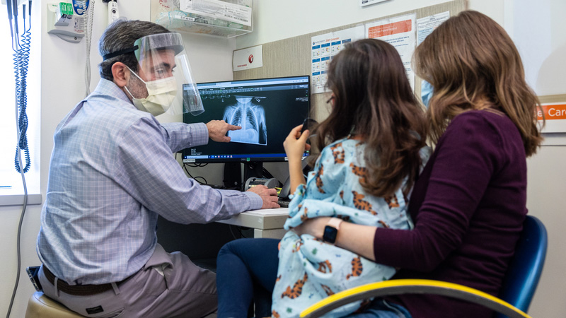 Dr. Cooper with a young girl and her mother in an exam room looking at a chest x-ray on a computer